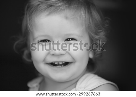 Portrait of little laughing pretty male kid with curly hair looking forward outdoor on dark background black and white closeup, horizontal picture