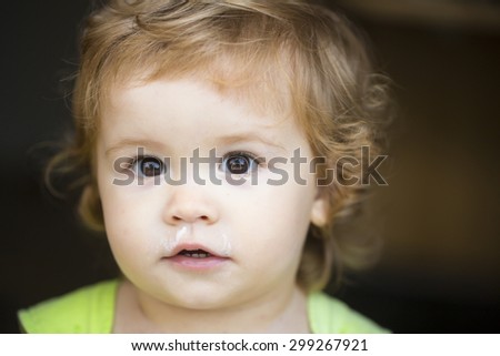 Portrait of small curious sweet male kid with blond curly hair looking forward outdoor on dark background, horizontal picture