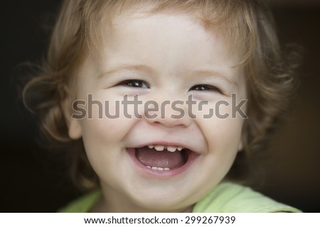 Portrait of small laughing cute male kid with blond curly hair looking forward outdoor on dark background, horizontal picture