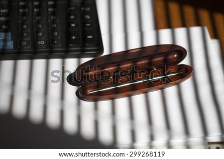 Elegant silver ball-point pen in brown wooden open case near black keyboard lying on white envelope and sheet of empty paper on office table on jalousie shadow background, horizontal picture