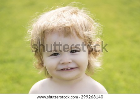 Portrait of small happy smiling male child with blonde curly hair looking forward outdoor sunny day on natural green background, horizontal picture