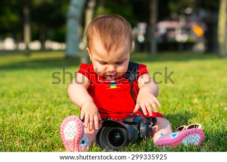 Baby girl is playing with DSLR camera on grass. Baby with camera