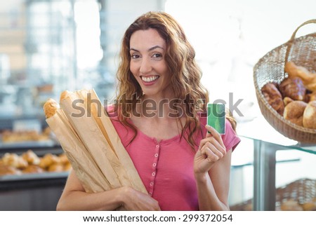 Pretty brunette holding credit card and baguettes at the bakery