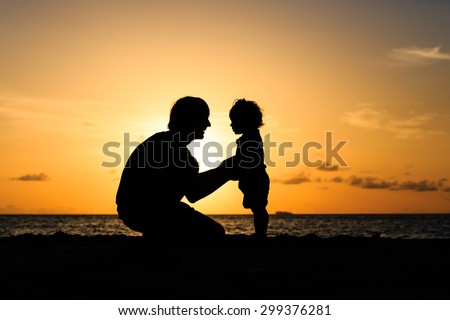 Father and little daughter silhouettes holding hands at sunset beach