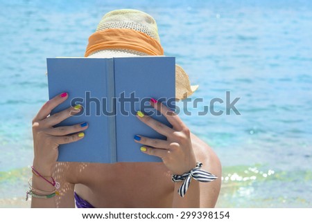 Girl with straw hat reading book on the beach on a sunny day