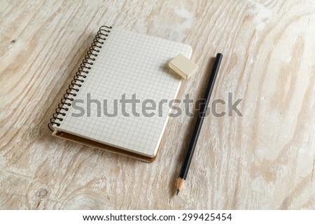 Notebook with a pencil and eraser on light wooden background with soft shadows. Template for graphic designers portfolios. Top view.