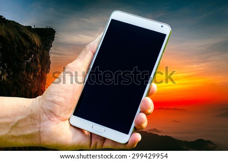 Man hand holding smartphone against on sunrise background soft focus.