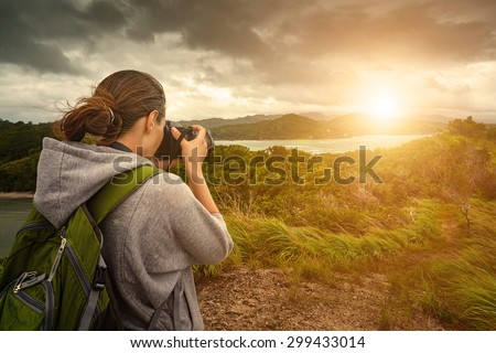 Travelling woman photographer with backpack  making an inspiring landscape of dramatic clouds. Tourist girl traveling along Asia, active lifestyle concept