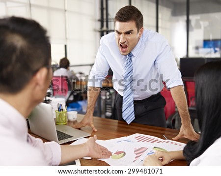 bad-tempered caucasian business executive yelling at two asian subordinates in office. Royalty-Free Stock Photo #299481071