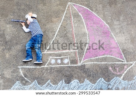 Creative leisure for children: Funny little boy of four years having fun with ship or boat picture drawing with chalk.