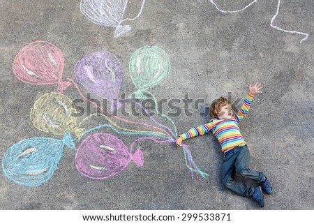 Happy little kid boy having fun with colorful balloons picture drawing with colorful chalks. Creative leisure for children outdoors in summer