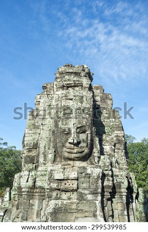 Angkor Wat Temple of Bayon stone face sculptures in front of green trees under blue sky 