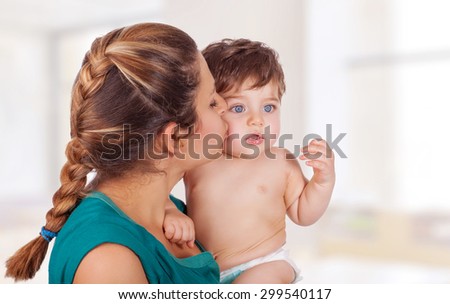 Portrait of happy young mother holding on hands cute little son and kissing him with love, with pleasure spending time at home, enjoying motherhood