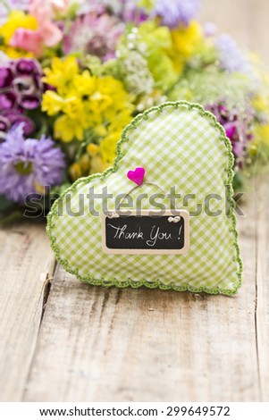 a green heart with a tag  saying: "Thank you" and a bouquet of flowers in the background