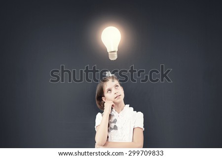 Cute thoughtful girl of school age standing near blackboard