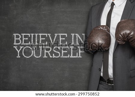 Believe in yourself on blackboard with businessman wearing boxing gloves
