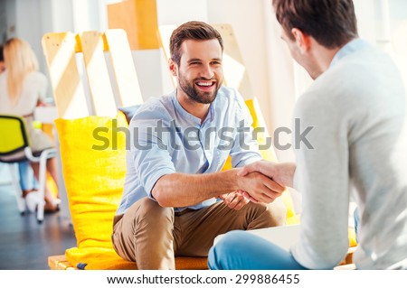 Sealing a deal! Two happy young men shaking hands while sitting in the rest area of the office Royalty-Free Stock Photo #299886455