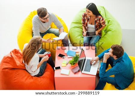 Place where ideas born. Top view of four young people working together while sitting at the colorful bean bags Royalty-Free Stock Photo #299889119