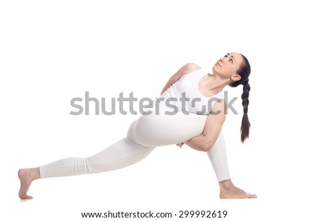 Sporty beautiful young woman in white sportswear doing lunge exercise for spine flexibility, standing in parivritta parshvakonasana variation with hands behind back, full length isolated studio shot