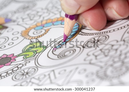 An image of a new trendy thing called adults coloring book. In this image a person is coloring an illustrative and detailed pattern for stress relieve for adults.