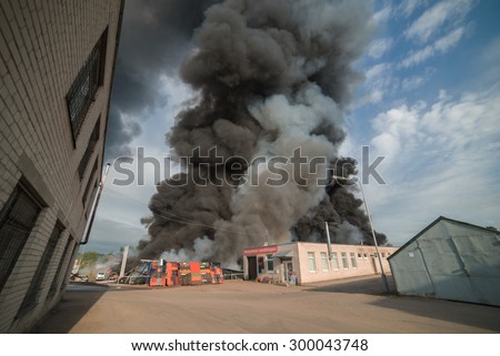 A Huge fire n the industrial area of the city. Buildings and cars in the fire. Open fire and black smoke going up to the sky. Picture taken with wide angle lens, representing necessity of insurance. 