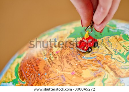 The girl rolls a little toy car on the globe