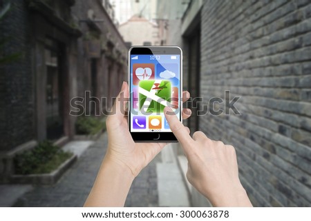 Woman left hand holding smart phone, right finger touching map icon, with daytime street background.
