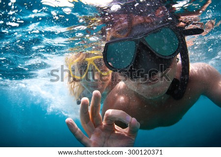 Young couple having fun underwater and showing ok sign