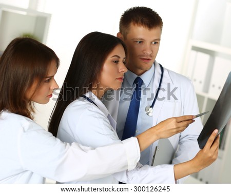 Three medicine doctors examining x-ray photography of patient to detect problem. Professional conversation, council of physicians. Working conference. Radiologist or traumatologist medical concept