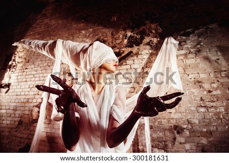 Closeup portrait of blind insane creature in cocoon stretching black hands towards watcher at bricks wall background. Concept of horror movie.