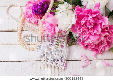 Decorative white heart, pearl and fresh pink and white peonies flowers on white painted wooden planks. Selective focus. Place for text. Toned image.
