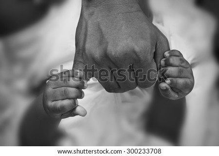 Hands of son holding his father's fingers. Black and white photography.