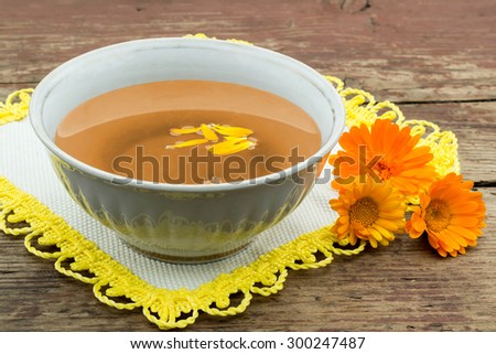 Herbal medicine: freshly brewed tea in a cup with calendula, marigold flowers on a napkin and a wooden rustic table