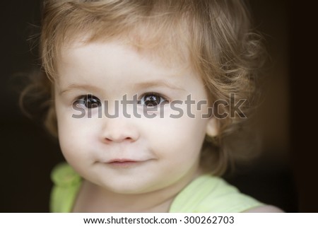 Portrait of little curious smiling male kid with blond curly hair looking forward outdoor on dark background, horizontal picture