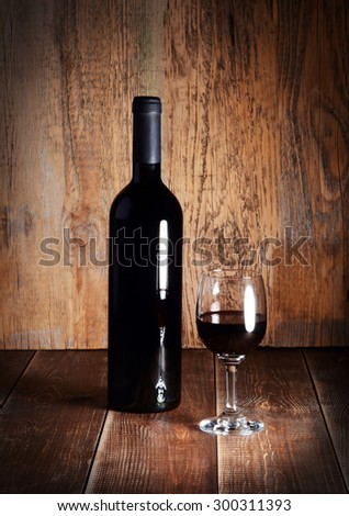 Bottle and glass of red wine on wooden table.