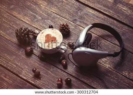 Cup of coffee with heart shape and headphones on wooden background