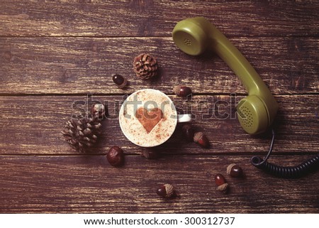 Cup of coffee with heart shape and green handset on wooden background