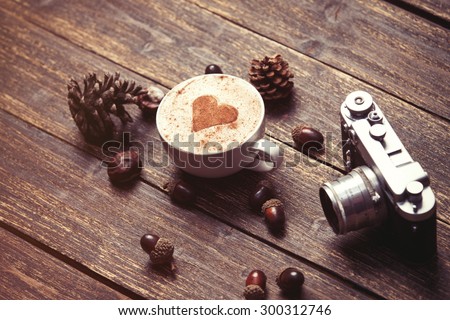 Cup of coffee with heart shape and pine cone with acorn and camera on wooden background
