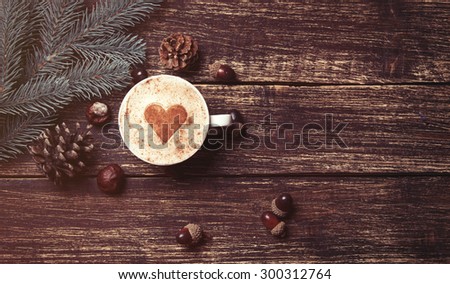Cup of coffee with heart shape and pine cone with acorn on wooden background