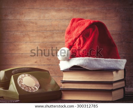 Santas hat over books near green dial phone on wooden background.