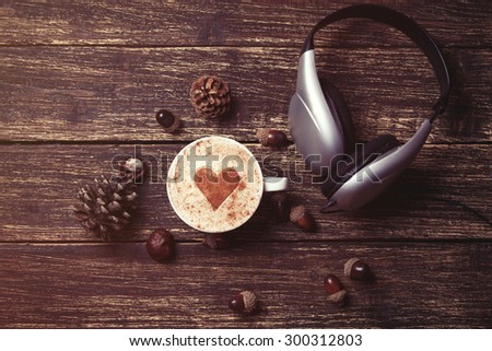 Cup of coffee with heart shape and headphones on wooden background