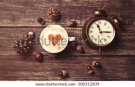 Cup of coffee with heart shape and pine cone with acorn and clock on wooden background