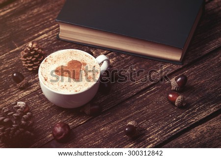 Cup of coffee with heart shape and pine cone with acorn, book on wooden background