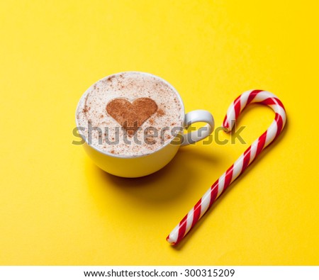 Cup of coffee with heart shape and christmas candy on yellow background.