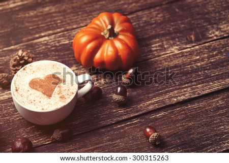Cup of coffee with heart shape and pine cone with acorn and pumpkin on wooden background