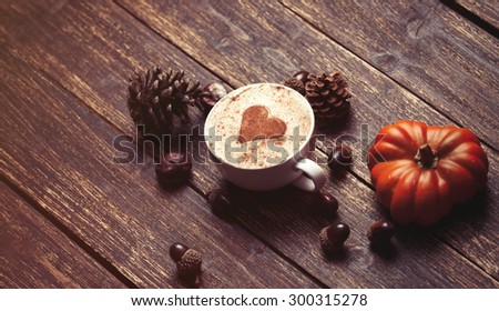 Cup of coffee with heart shape and pine cone with acorn and pumpkin on wooden background