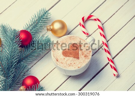Cup of coffee with heart shape and christmas candy near brench on white wooden background.