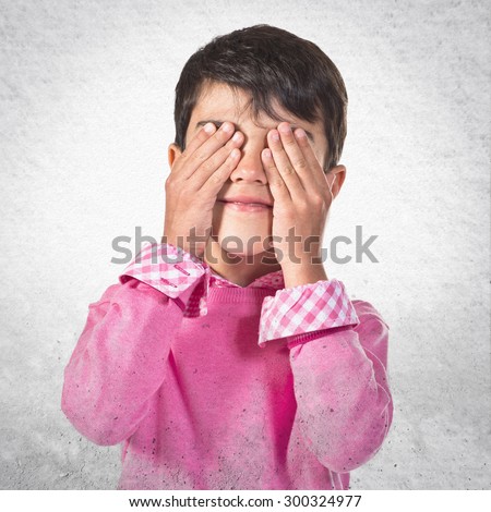 Kid covering his eyes over grey background