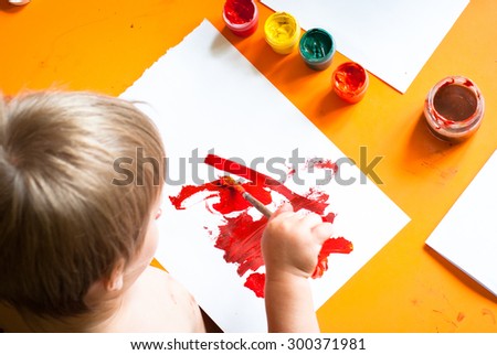 Little boy draws a brush and paint his first picture. Focus at the drawing