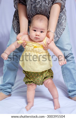 asian baby girl in traditional thai dress, her mom try to pull her stand and  she looking at the camera